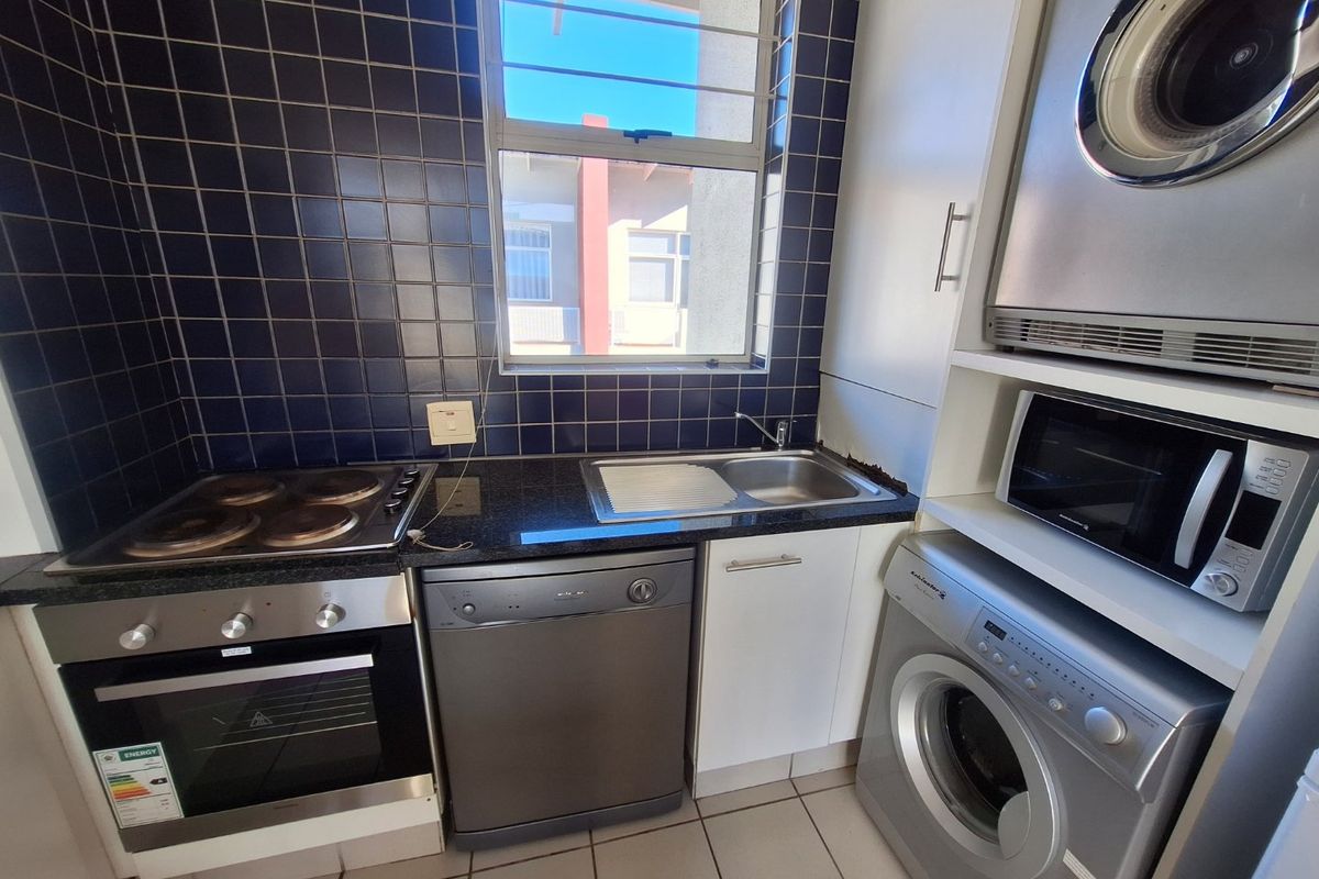 Compact kitchen featuring built-in oven, electric hob, stainless steel sink, granite countertops, and dark tiled backsplash with integrated laundry appliance space.