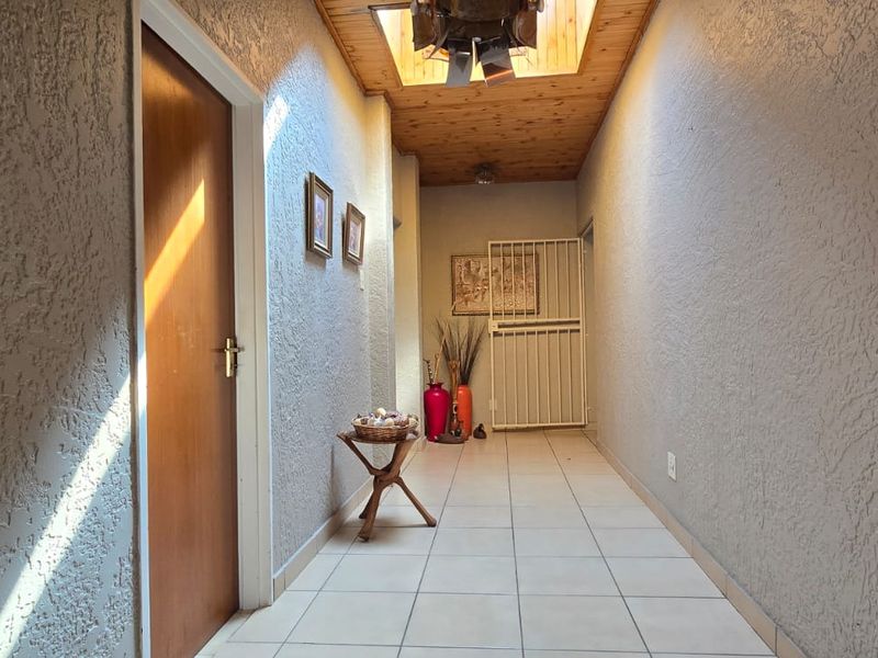 A well-lit hallway featuring textured walls, tiled flooring, and a timber-paneled ceiling with a security gate at the end.