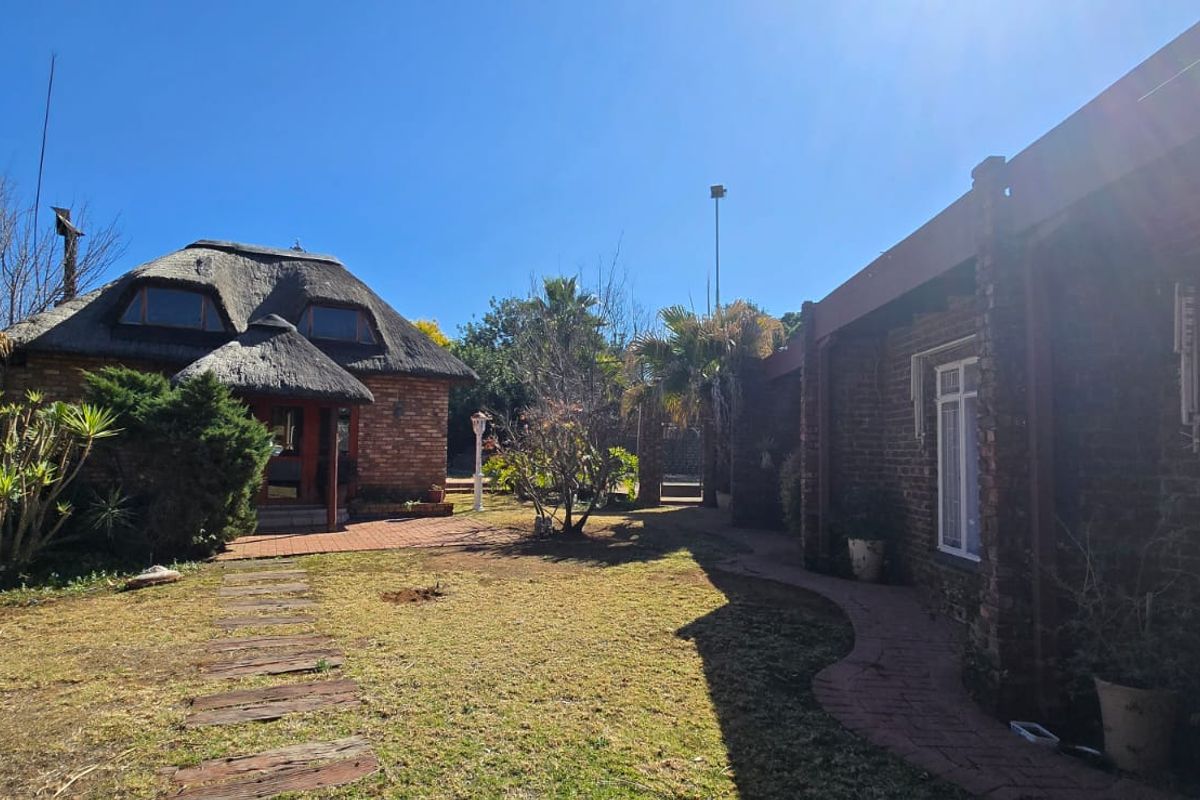 A view of the rear garden featuring a thatched roof structure, brick exterior walls, and a paved walkway connecting the outdoor spaces.