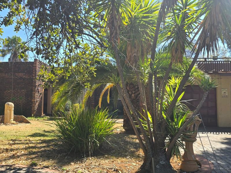 Front view of the property featuring a brick facade, paved driveway, and established garden area.