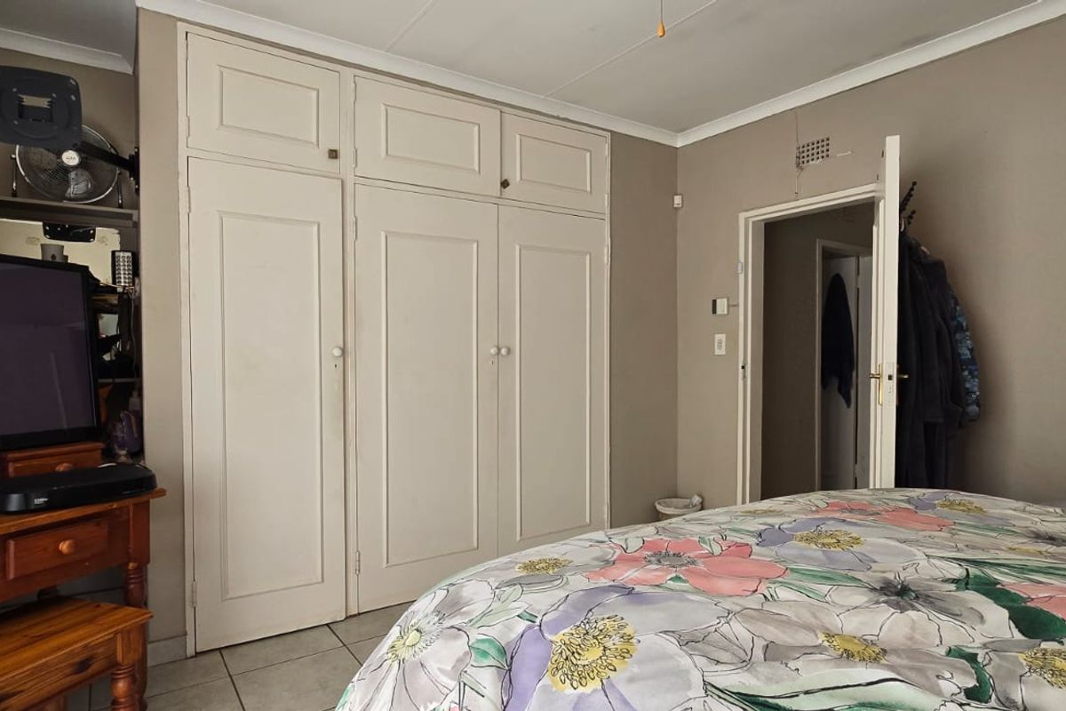 A bedroom featuring built-in cupboards, tiled flooring, and a coved ceiling, providing a functional and neutral living space.