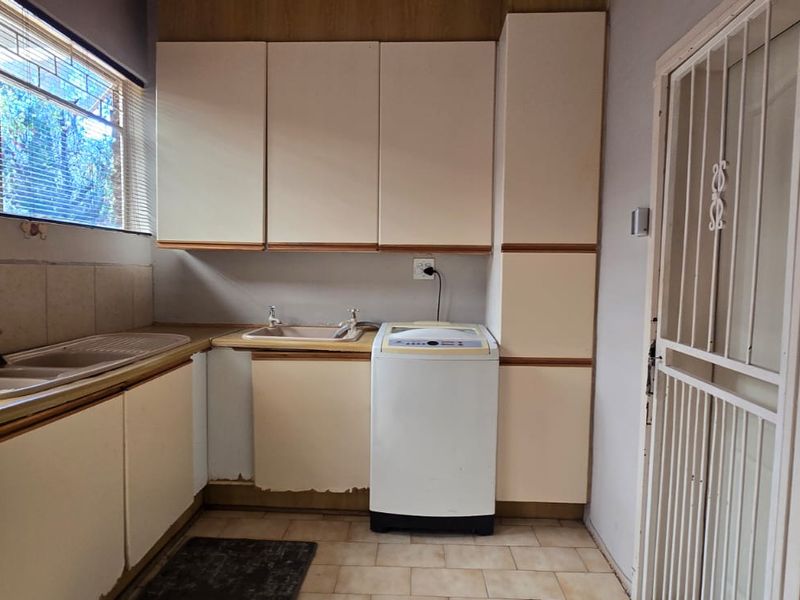 A functional scullery area featuring double sinks, laminate cabinetry, and tiled splashbacks, providing additional utility space with direct access via a security gate.