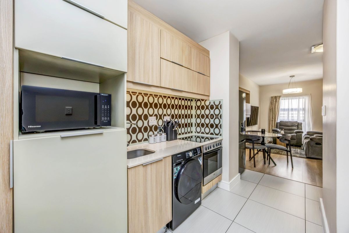 Modern open-plan kitchen featuring light wood cabinetry, integrated appliances, and a stylish patterned backsplash, flowing seamlessly into the adjacent living and dining area.