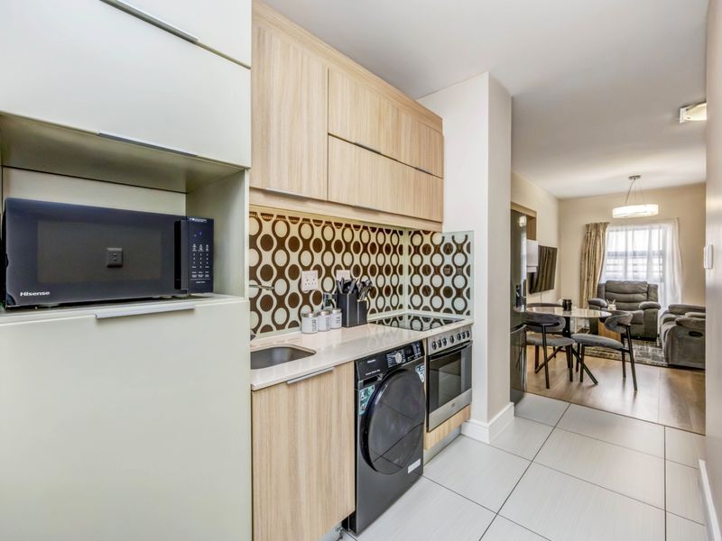 Modern open-plan kitchen featuring light wood cabinetry, integrated appliances, and a stylish patterned backsplash, flowing seamlessly into the adjacent living and dining area.