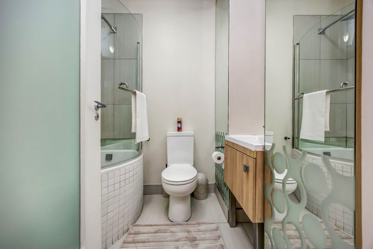 A compact, modern bathroom featuring a corner shower enclosure, a wall-mounted vanity with basin, and a toilet, finished with neutral tiles and glass partitions.