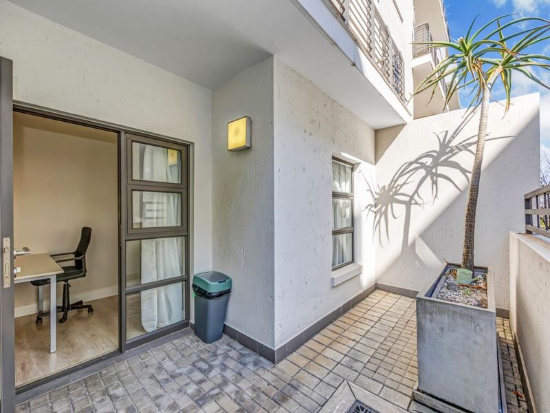 A private balcony featuring paved flooring, a built-in concrete planter, and direct access to an interior room through a sliding glass door.