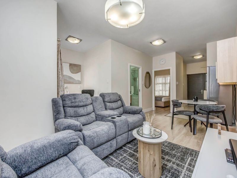 An open-plan living and dining area featuring neutral walls, laminate flooring, and recessed ceiling lighting, providing a functional and well-lit living space.