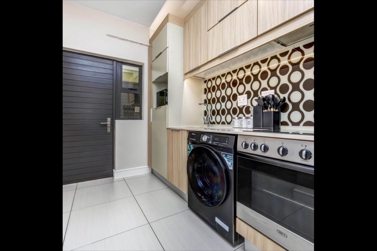 Modern kitchen featuring light wood cabinetry, a patterned splashback, integrated oven and hob, and tiled flooring.