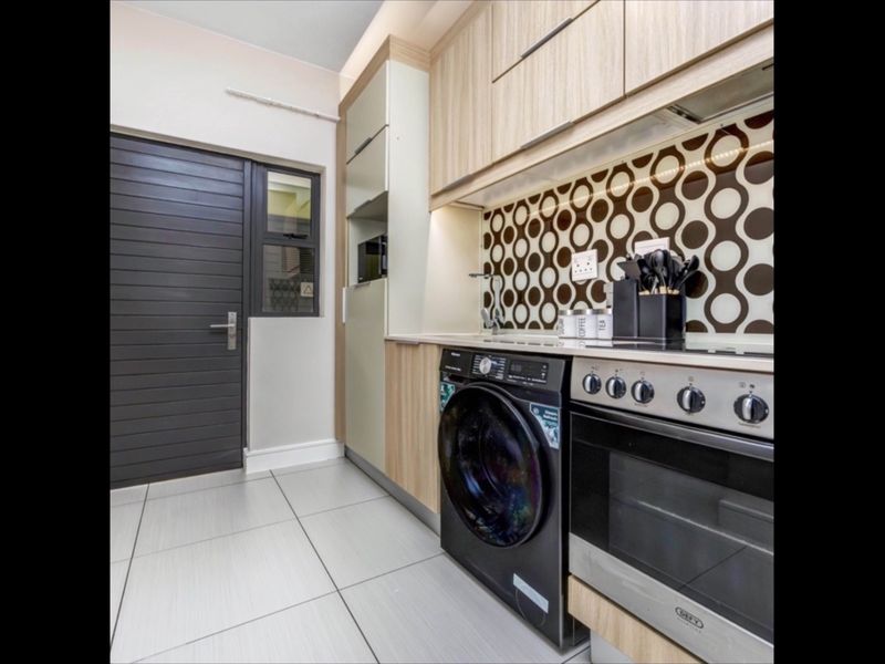 Modern kitchen featuring light wood cabinetry, a patterned splashback, integrated oven and hob, and tiled flooring.