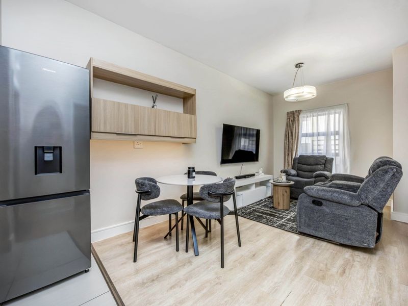 A well-maintained open-plan living and dining area featuring light laminate flooring, modern wall-mounted cabinetry, and neutral finishes throughout.