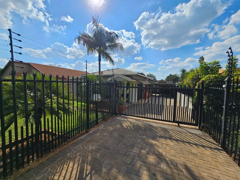 Front view of the property featuring a secure gated entrance, paved driveway, and perimeter electric fencing.