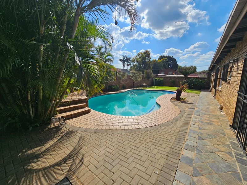 Outdoor pool area featuring a curved swimming pool with brick paving and a surrounding brick boundary wall.