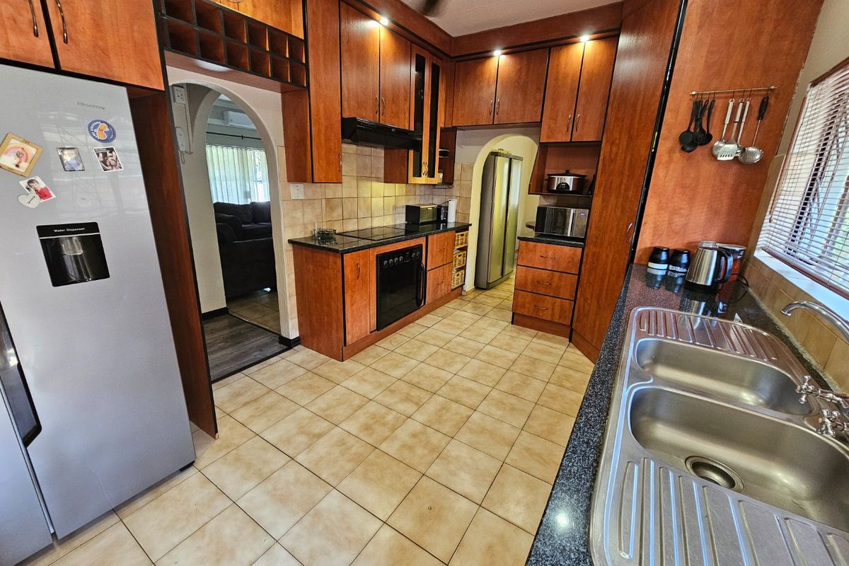 A functional kitchen featuring wooden cabinetry, granite countertops, a double stainless steel sink, and built-in cooking appliances with an adjacent scullery area.