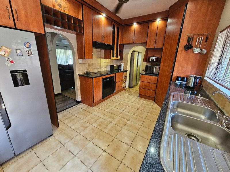 A functional kitchen featuring wooden cabinetry, granite countertops, a double stainless steel sink, and built-in cooking appliances with an adjacent scullery area.