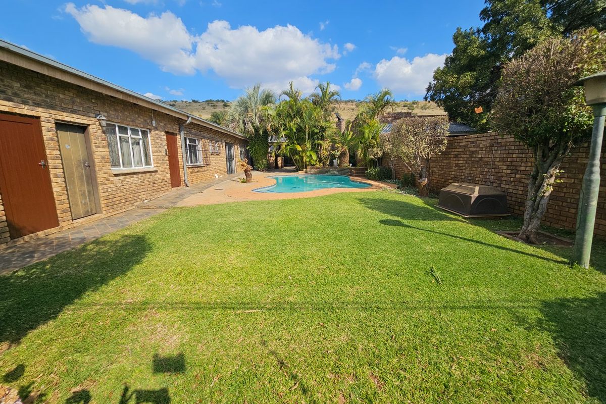 A spacious rear garden featuring a swimming pool, paved patio area, and established brick boundary walls.