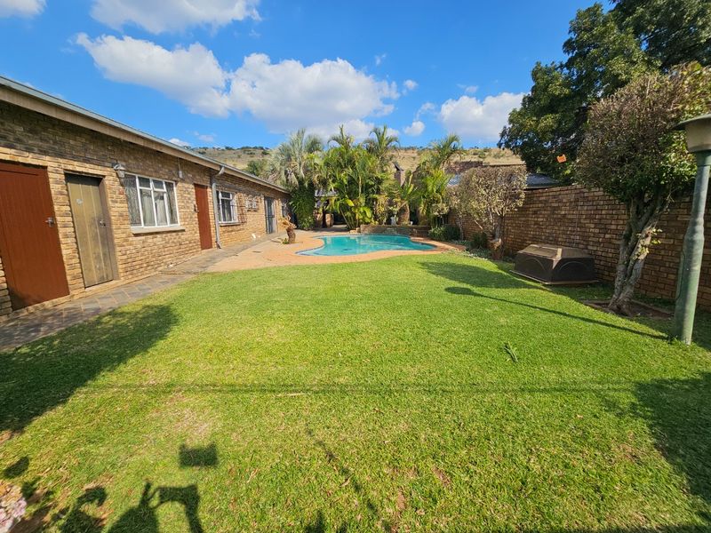 A spacious rear garden featuring a swimming pool, paved patio area, and established brick boundary walls.