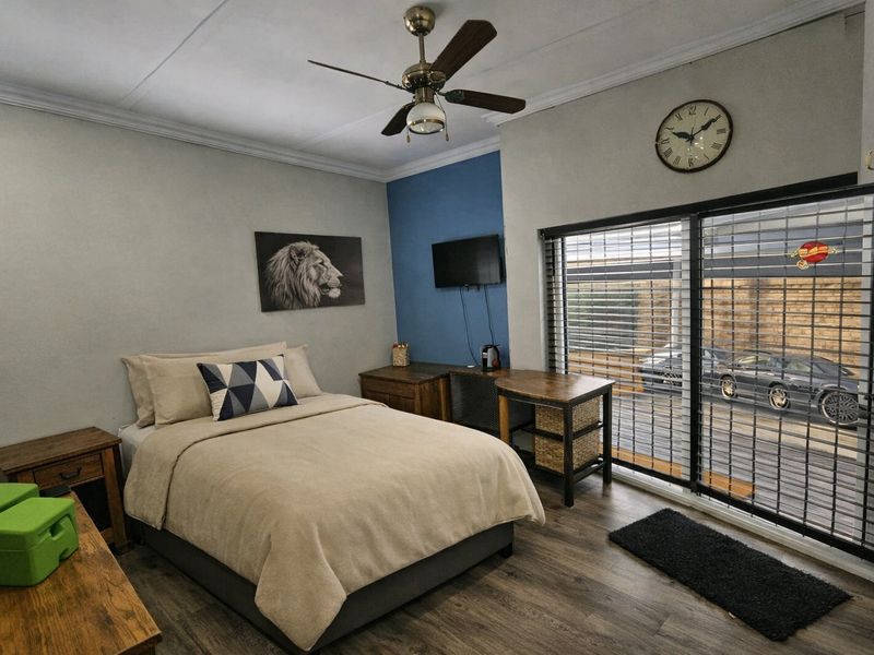 A well-maintained bedroom featuring laminate flooring, a ceiling fan, and a sliding glass door with an integrated security gate providing exterior access.