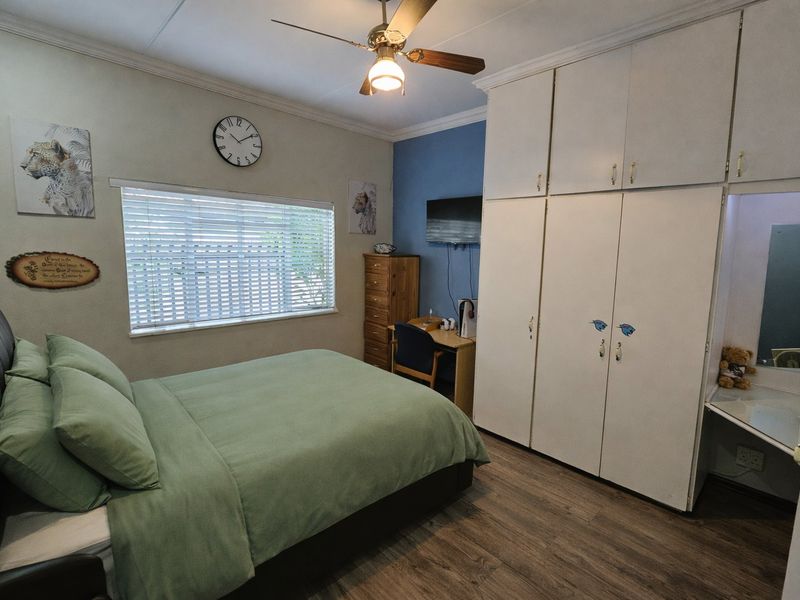 A functional bedroom featuring built-in cupboards, laminate flooring, and a ceiling fan, offering a comfortable and practical living space.