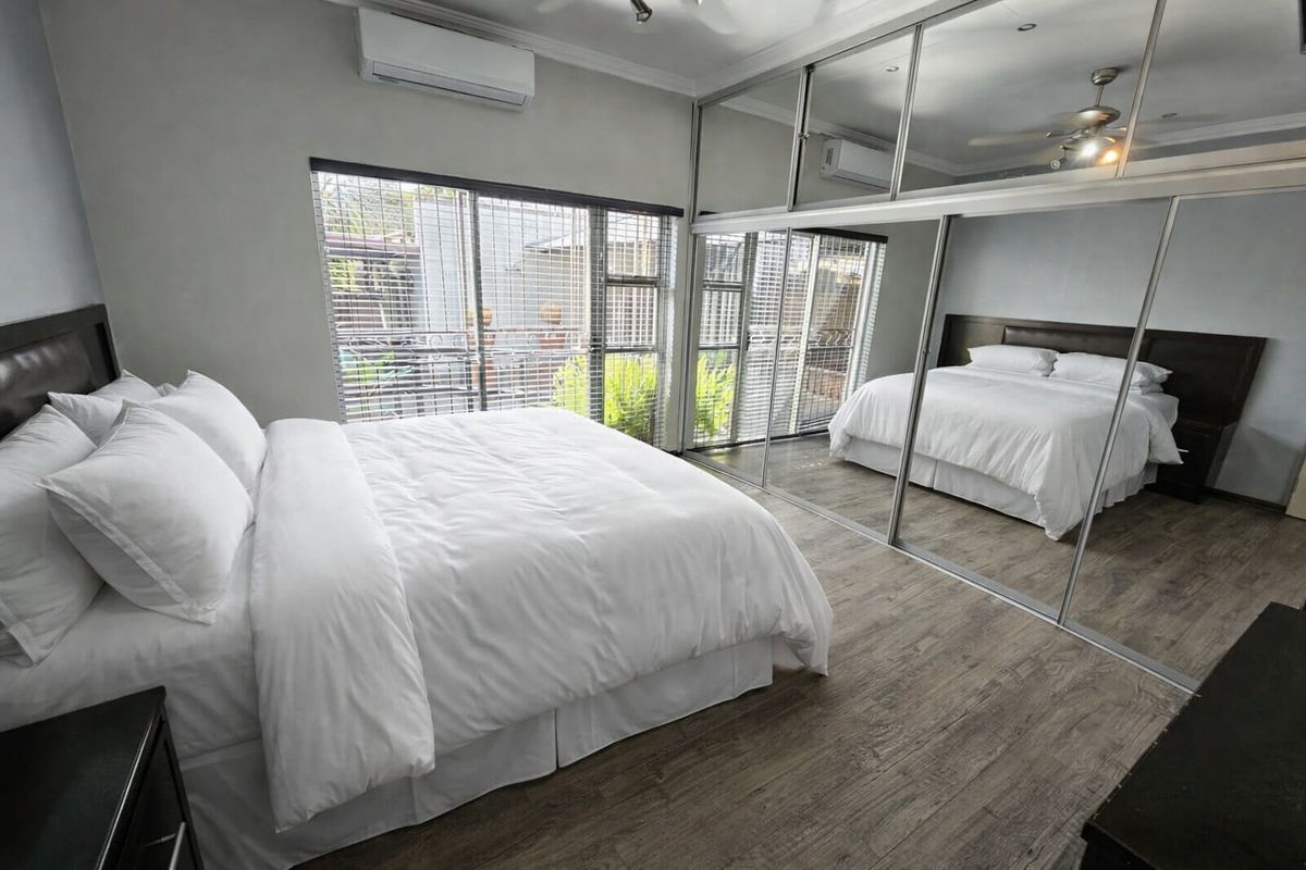 Spacious bedroom featuring laminate flooring, a large built-in mirrored wardrobe, ceiling fan, and a wall-mounted split-system air conditioner.