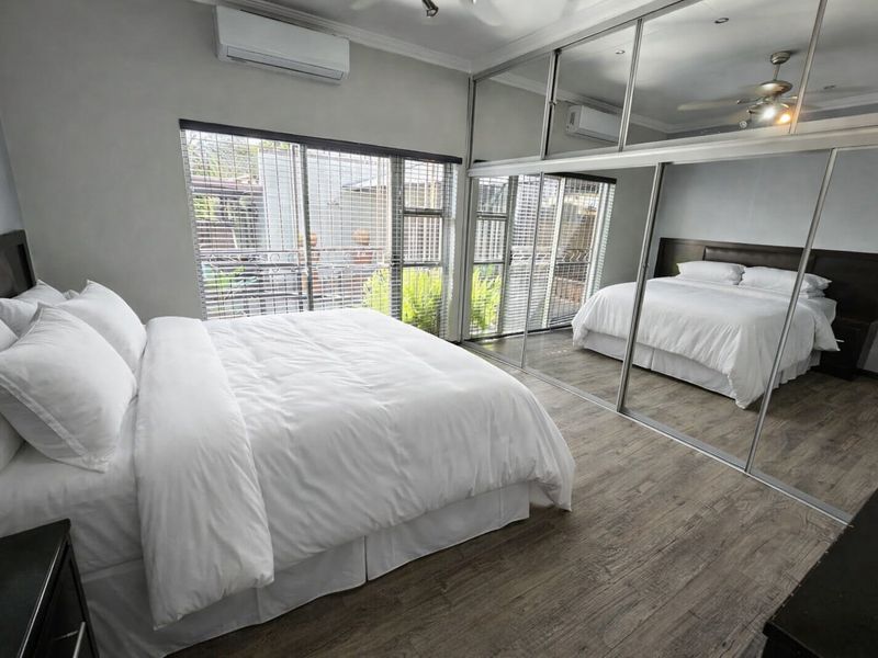 Spacious bedroom featuring laminate flooring, a large built-in mirrored wardrobe, ceiling fan, and a wall-mounted split-system air conditioner.