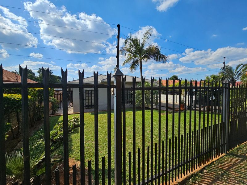 Front view of the property featuring a well-maintained lawn, secure metal fencing, and electric security wiring.