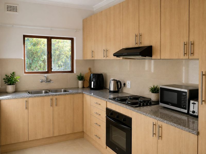 A well-maintained kitchen featuring light wood-finish cabinetry, granite countertops, a double basin sink, and integrated appliances including an oven and hob.