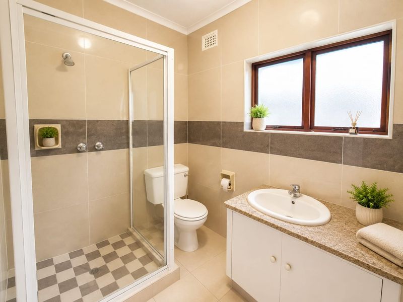 A well-maintained bathroom featuring a glass-enclosed shower, a vanity with a granite countertop, and neutral wall tiling.