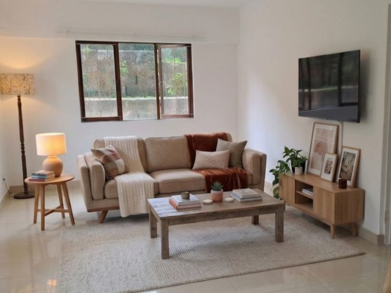 A bright and well-maintained living room featuring neutral tiled flooring and a large casement window providing natural light.