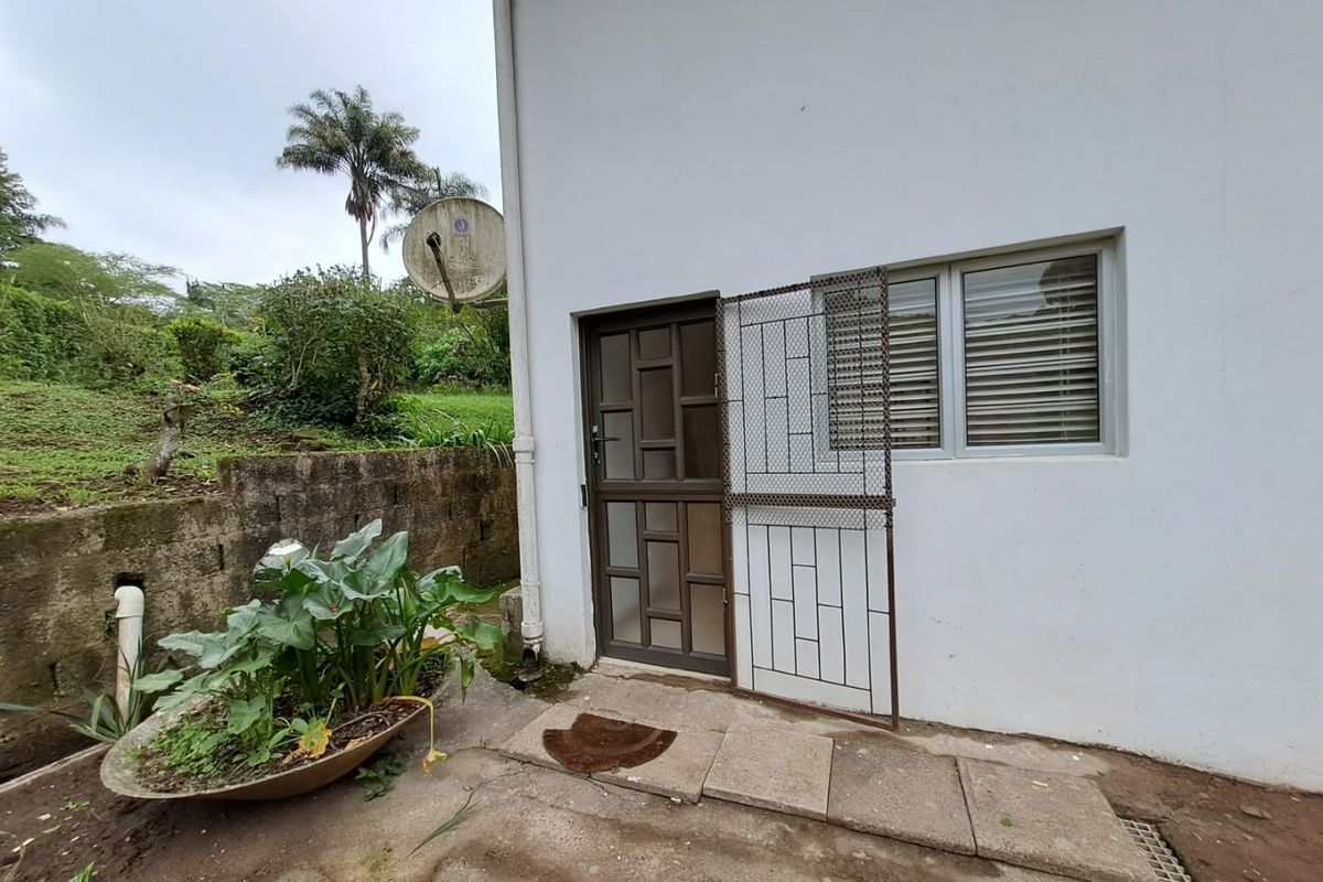 Rear exterior view of the apartment featuring a security gate, aluminium window, and paved access area with a retaining wall.