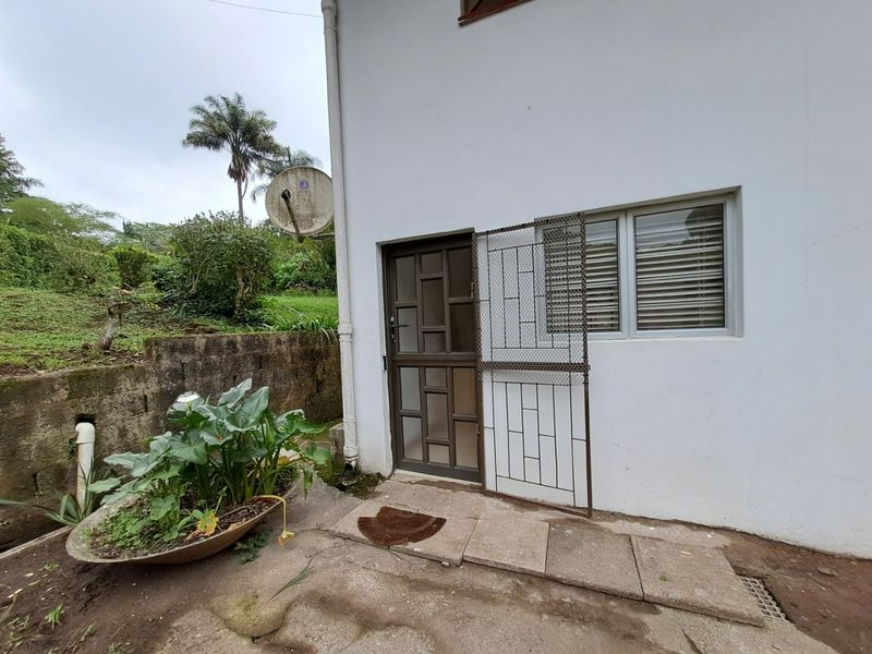 Rear exterior view of the apartment featuring a security gate, aluminium window, and paved access area with a retaining wall.