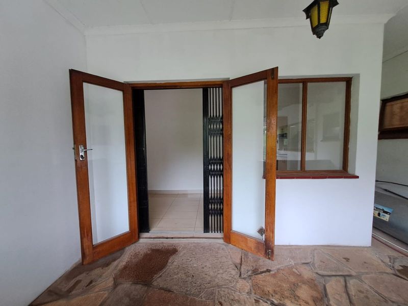 Covered patio area featuring stone paving, wooden framed glass doors, and a security gate leading into the apartment interior.