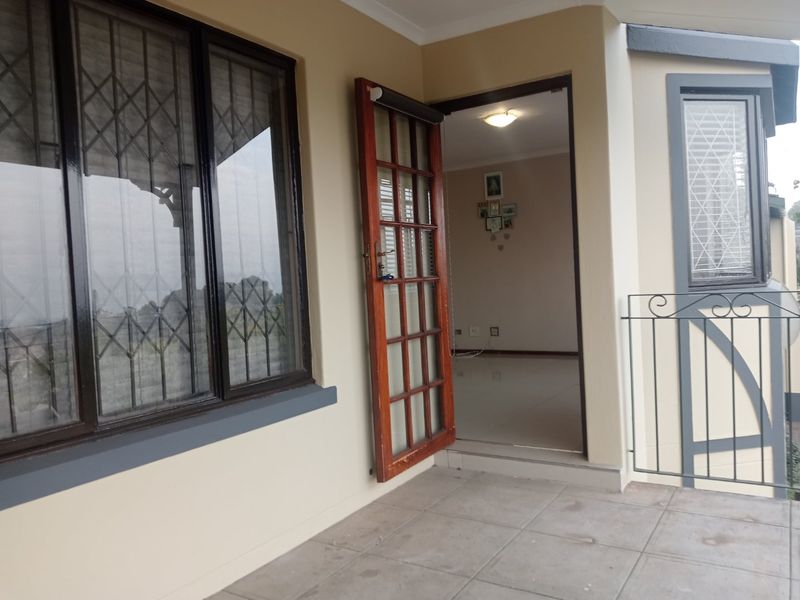 A covered balcony area featuring tiled flooring, a timber-framed glass door, and metal security bars, providing access to the interior living space.