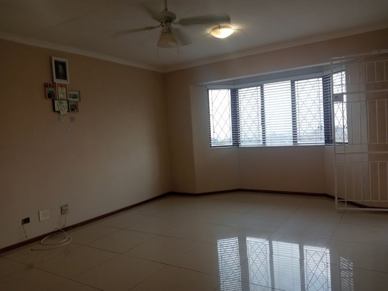 Spacious living area featuring large bay windows with security gates, tiled flooring, and a ceiling fan, offering a bright and neutral blank canvas.