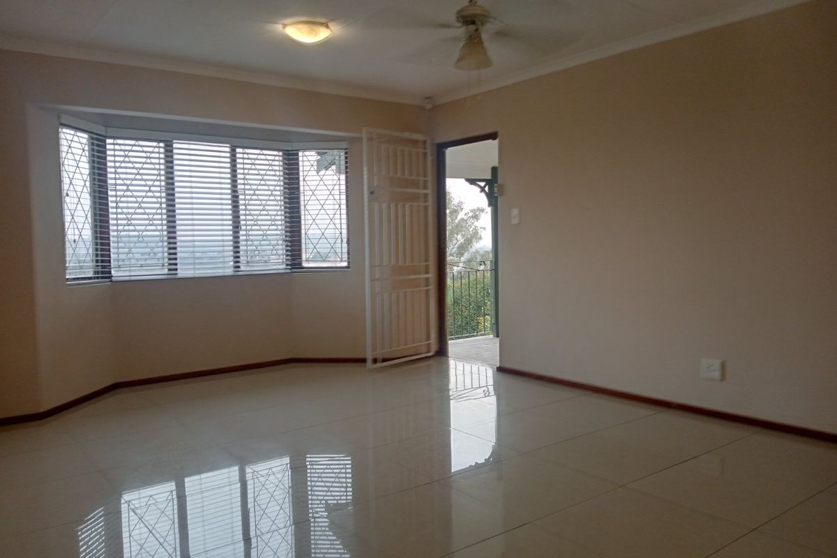 A spacious, empty living room featuring tiled flooring, a ceiling fan, and a large bay window with access to an outdoor balcony area.