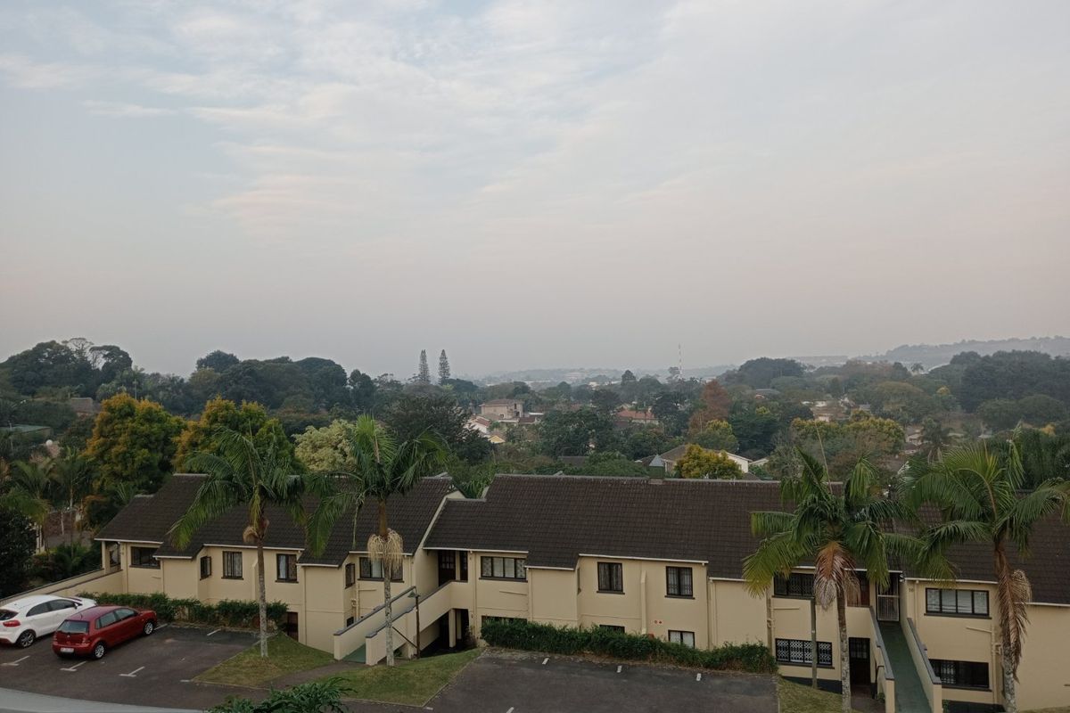 An elevated aerial view of an apartment complex featuring tiled roofs, paved parking areas, and established garden landscaping with palm trees.