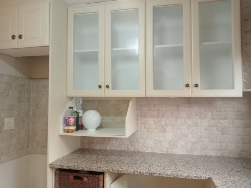 A functional kitchen area featuring granite countertops, tiled backsplash, and glass-fronted upper cabinetry providing ample storage space.