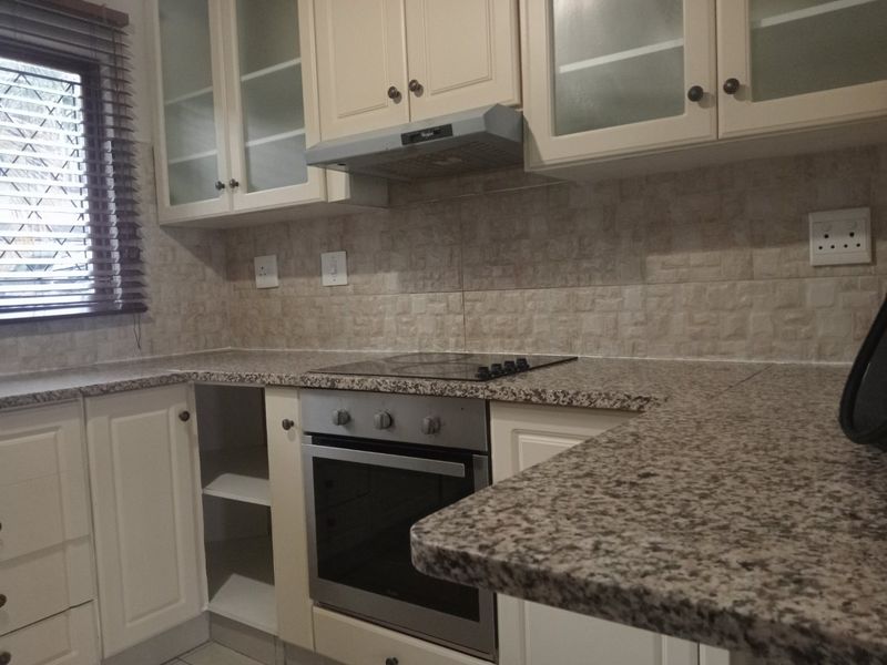 A functional kitchen featuring granite countertops, built-in oven, electric hob, extractor fan, and ample shaker-style cabinetry with a tiled backsplash.