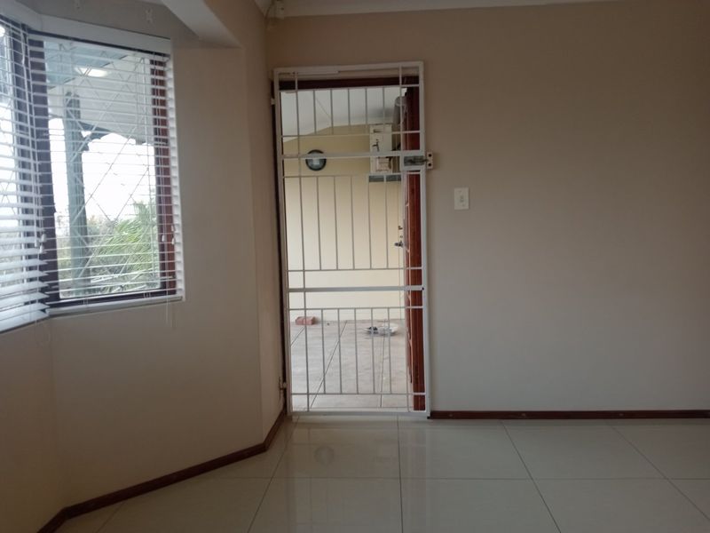 An empty living area featuring tiled flooring, venetian blinds, and a security gate leading to an outdoor space.