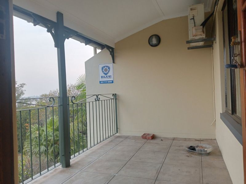 A covered balcony featuring tiled flooring, wrought iron railings, and an external air conditioning unit, offering an outdoor space with elevated views.