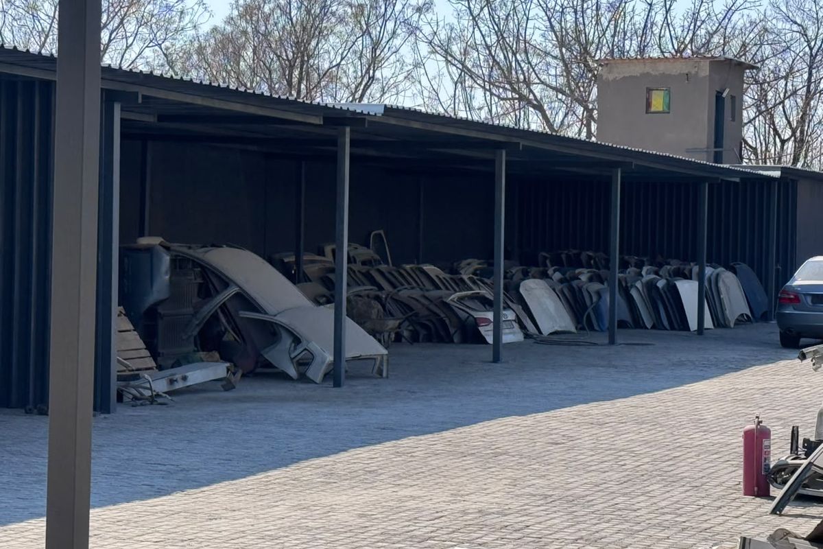 A large industrial covered parking area with steel structural supports and paved flooring, currently utilized for storage.