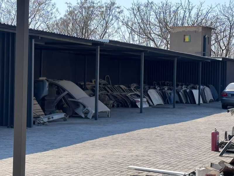 A large industrial covered parking area with steel structural supports and paved flooring, currently utilized for storage.