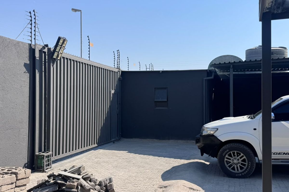 Secure industrial yard area featuring a paved driveway, steel sliding gate, electric fencing, and a water storage tank.