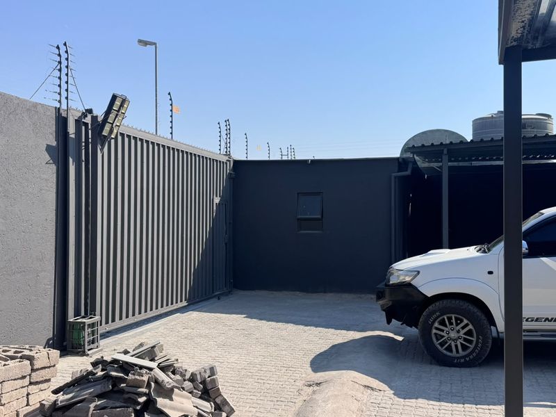 Secure industrial yard area featuring a paved driveway, steel sliding gate, electric fencing, and a water storage tank.