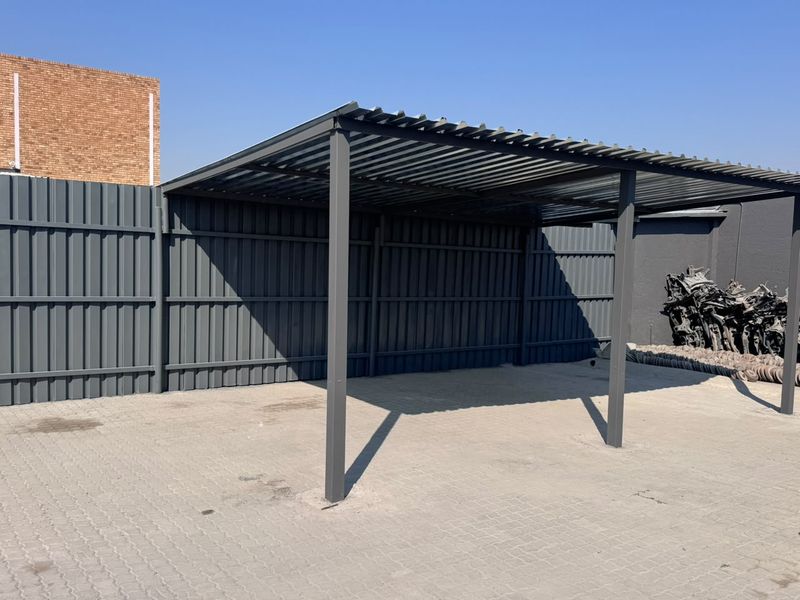 A functional outdoor covered parking structure featuring a durable corrugated metal roof, steel support posts, and paved ground surface.
