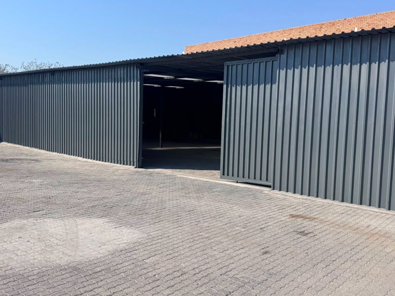 A large industrial garage featuring corrugated metal cladding, a wide sliding entrance door, and a paved exterior apron.