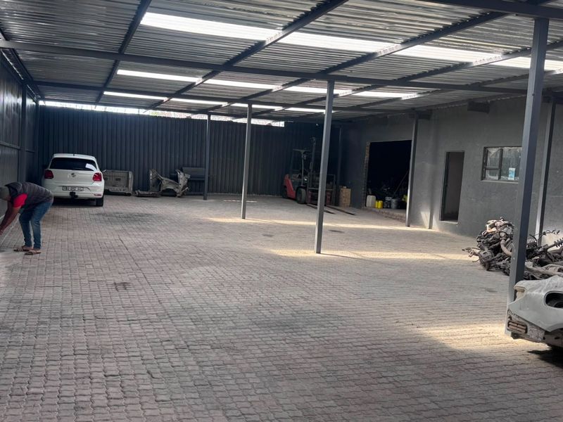 Spacious industrial garage area featuring a covered roof structure, steel support columns, and durable paved flooring, suitable for vehicle storage or workshop operations.