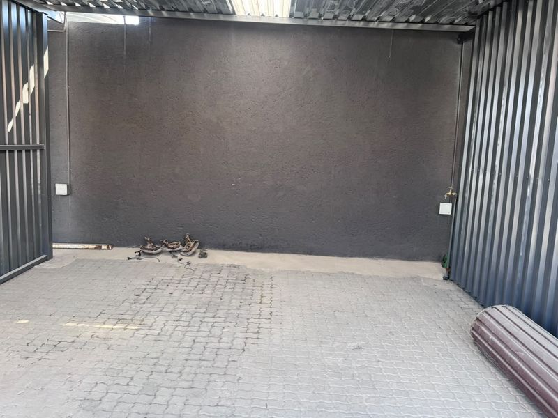 A functional industrial garage space featuring durable paved flooring, corrugated metal wall cladding, and a convenient external water tap.