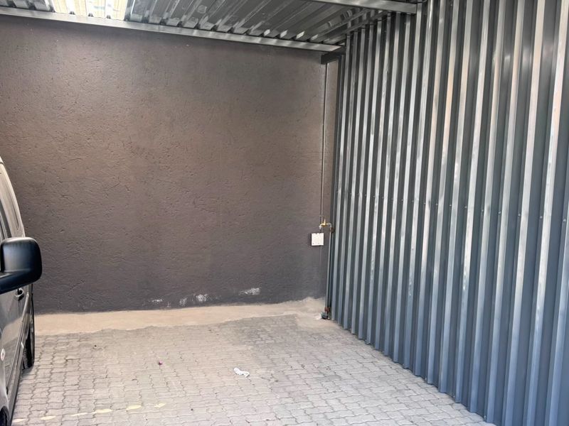 A functional industrial garage space featuring corrugated metal walls and roof with durable paver flooring and an integrated water tap.