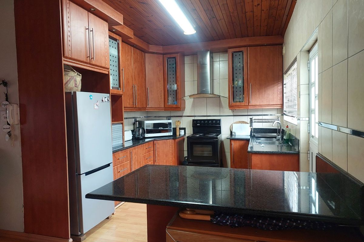 A functional kitchen featuring wooden cabinetry, granite countertops, a stainless steel extractor fan, and a tiled backsplash with a warm wooden ceiling finish.