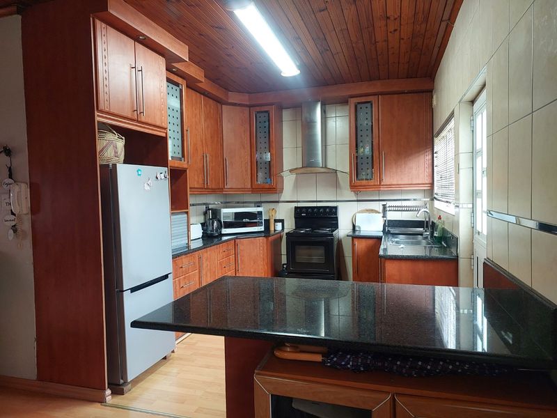 A functional kitchen featuring wooden cabinetry, granite countertops, a stainless steel extractor fan, and a tiled backsplash with a warm wooden ceiling finish.